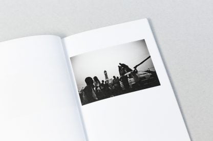 Otwarta książka z czarno-białym zdjęciem grupy ludzi na tle samochodu.