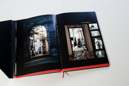 Otwarta książka, na czarnych stronach zdjęcia z wystawy Shadows of Humor.