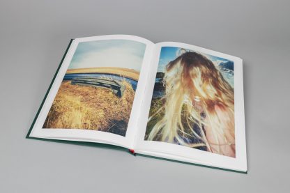 Kolorowe zdjęcia wewnątrz książki. Po lewej wysuszona trawa, w tle woda, po prawej długie włosy blond.