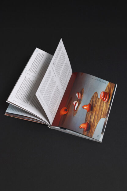 Open SIC! - a book about the SIC! Gallery BWA Wrocław on a dark surface, showing pages with text on the left and a photograph of orange ceramic objects on the right.