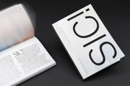 Two thick white books lie on a dark surface, one opened to show black printed text and another closed with the product name "SIC! - a book about the SIC! Gellery BWA Wrocław" prominently displayed on the cover in large black letters.